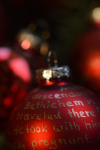 The Nativity story written in golden letters on red Christmas ornament bulbs. 
