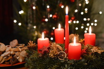 Five candles are burning at the Advent wreath for christmas day in front of a chrismas tree and next to a plate with christmas cookies