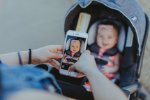 a mother taking a picture of her baby in a stroller with her smartphone 