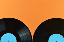two old black vinyl records with blank cyan labels on orange background