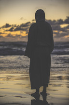 Jesus in a robe standing on a shore at sunset 