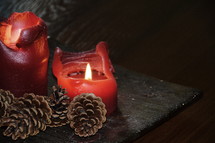 red candles with melting wax and pine cones 