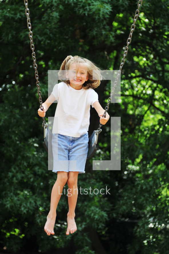 Girl swinging outside by trees.