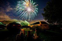 bursting fireworks in the night sky over parked cars 