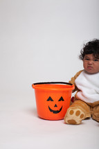 a toddler boy in a Halloween costume with a jack-o-lantern bucket 