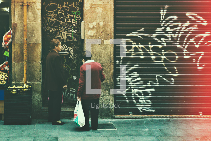 elderly women talking on a sidewalk in front of graffiti 