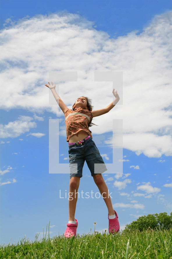 young girl jumping up in the air on a hillside