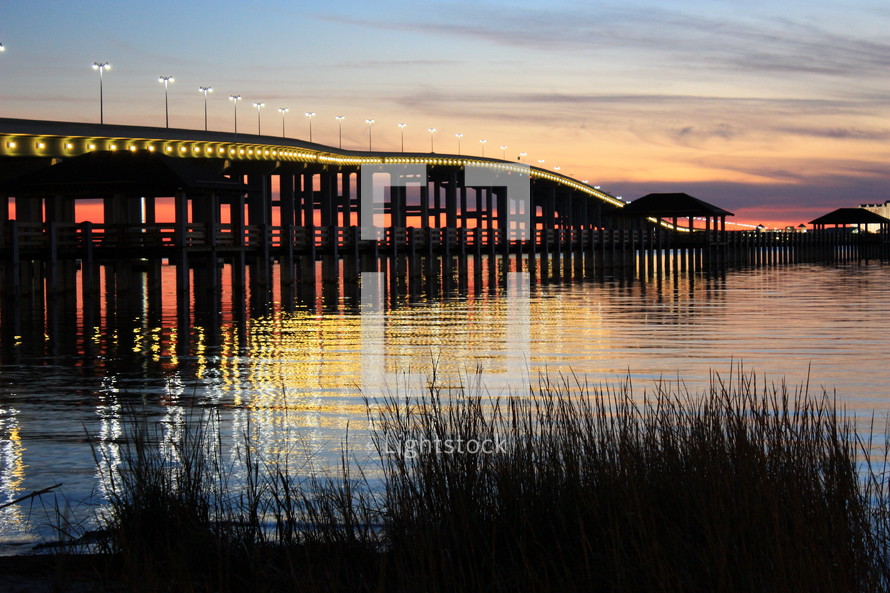 a lighted bridge over water, a red sunset in the distance