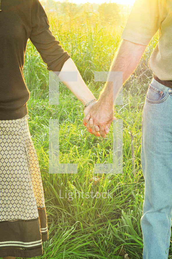 Couple holding hands while standing in tall grass.
