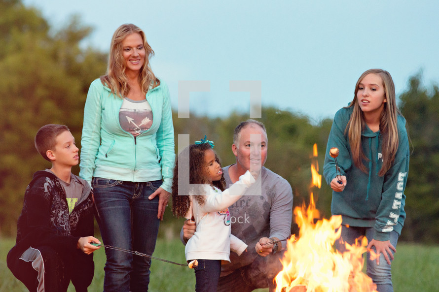 a family standing by a camp fire roasting marshmallows 
