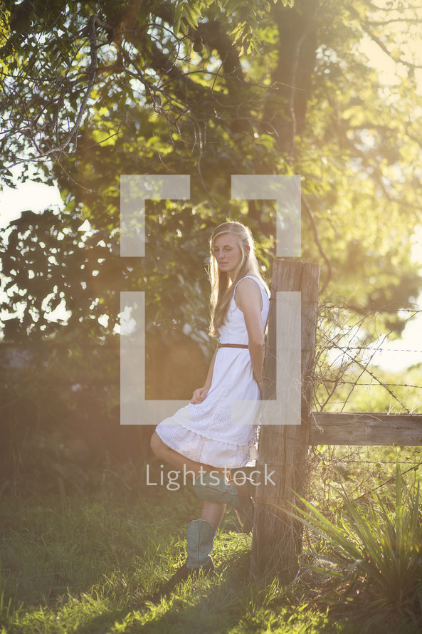 woman in cowboy boots leaning on a fence post 
