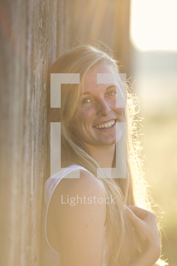 smiling woman leaning against a barn 