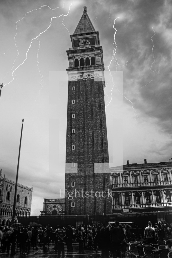 Lightning striking behind steepled tower with crowd on the ground.