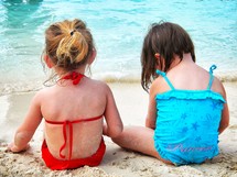 girls sitting on the beach in their bathing suits