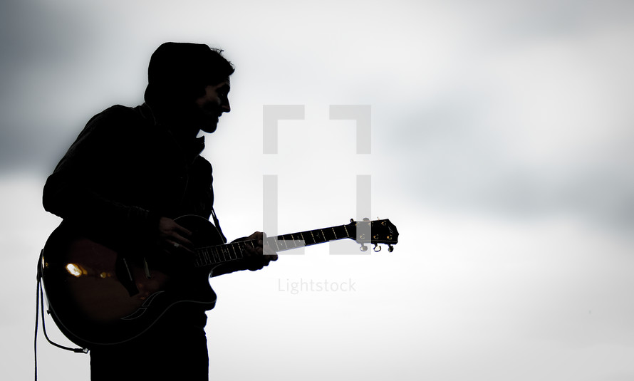 Silhouette of man playing guitar at dusk.