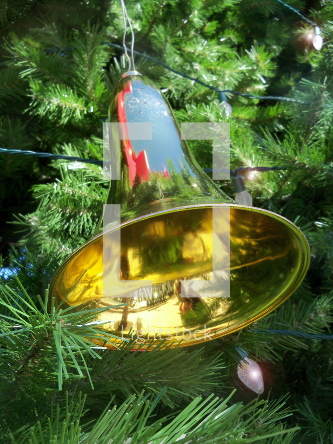 A brass Christmas bell decoration hanging on a Christmas tree reflecting the colors and glory of the Christmas season.