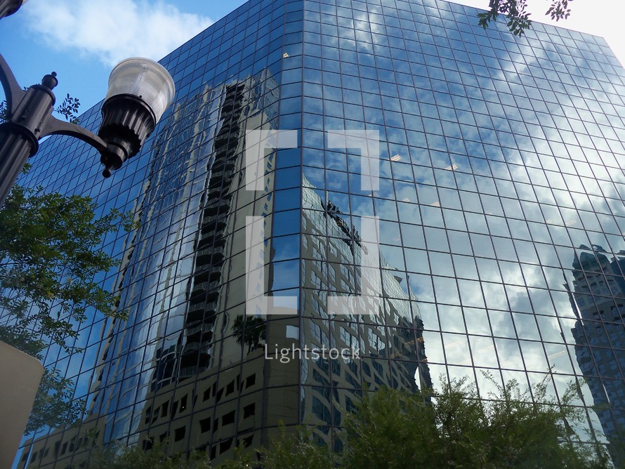 A City of glass reflection in downtown city showing the sky and reflecting cityscape surrounding its mirrored façade contrasting the old and the new corporate glass buildings with old architecture as cities grow and expand.