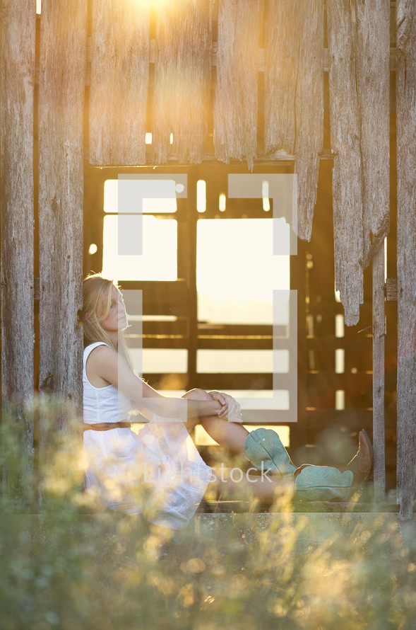 woman sitting in the window of an old weathered barn 