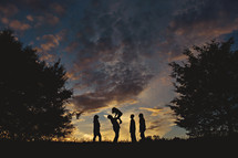 a silhouette of a family standing outdoors under an evening sky 