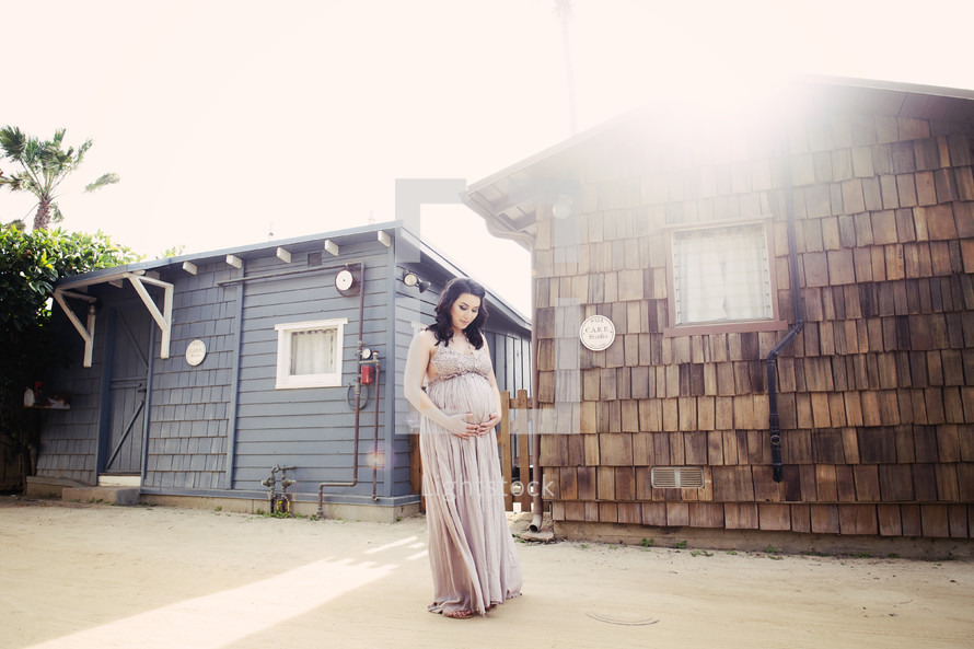 a pregnant woman standing in front of a house holding her belly 