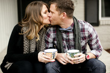 couple kissing holdig mugs of coffee 