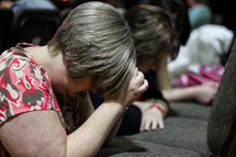 women kneeling in prayer in front of their seats at church 