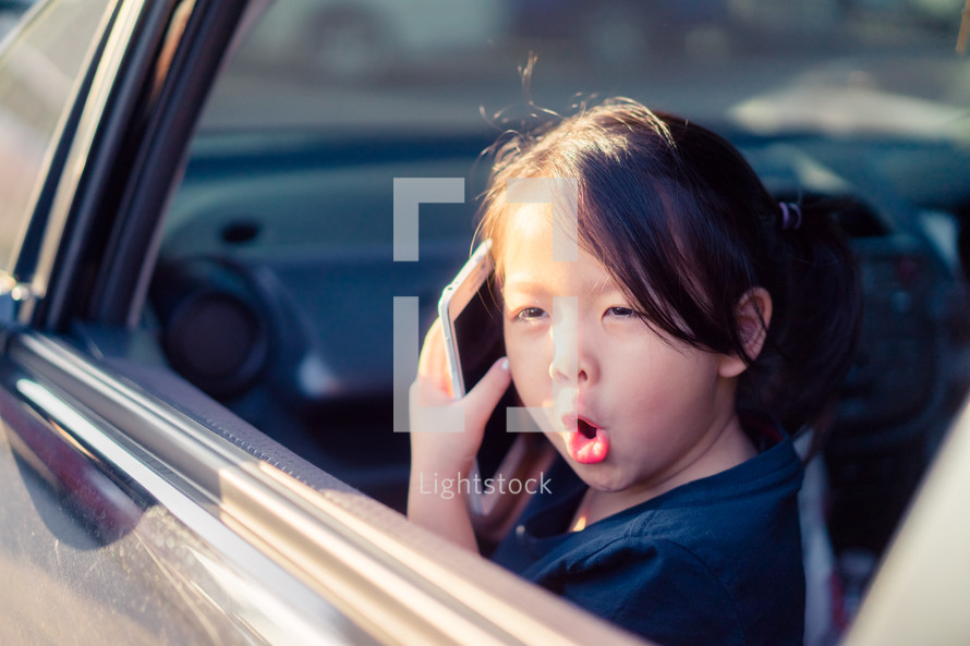 a little girl talking on a cellphone sitting in a car 