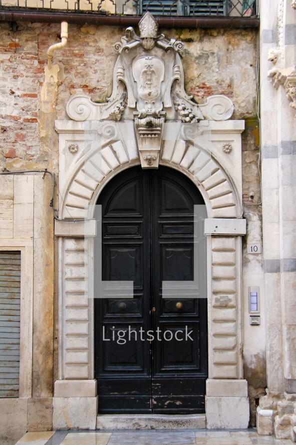 Arched black church doors in stone archway with Catholic emblem over