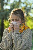 Girl in fall autumn sneezing in tissue