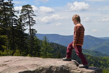 a child climbing to the top of a rock on a mountaintop 