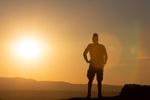 silhouette of a man standing at the edge of a mountain at sunset looking up 