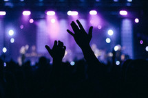 Silhouettes of raised hands at a concert.