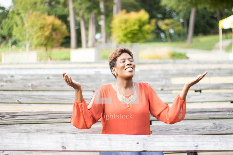 a woman sitting on a bench with raised hands praising God 