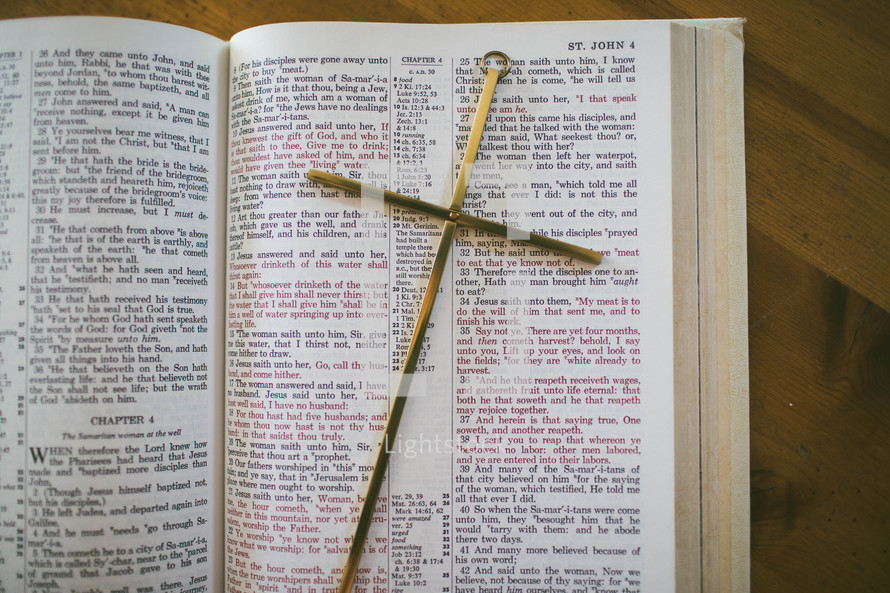 A brass cross laying on a Bible open to the Book of John.