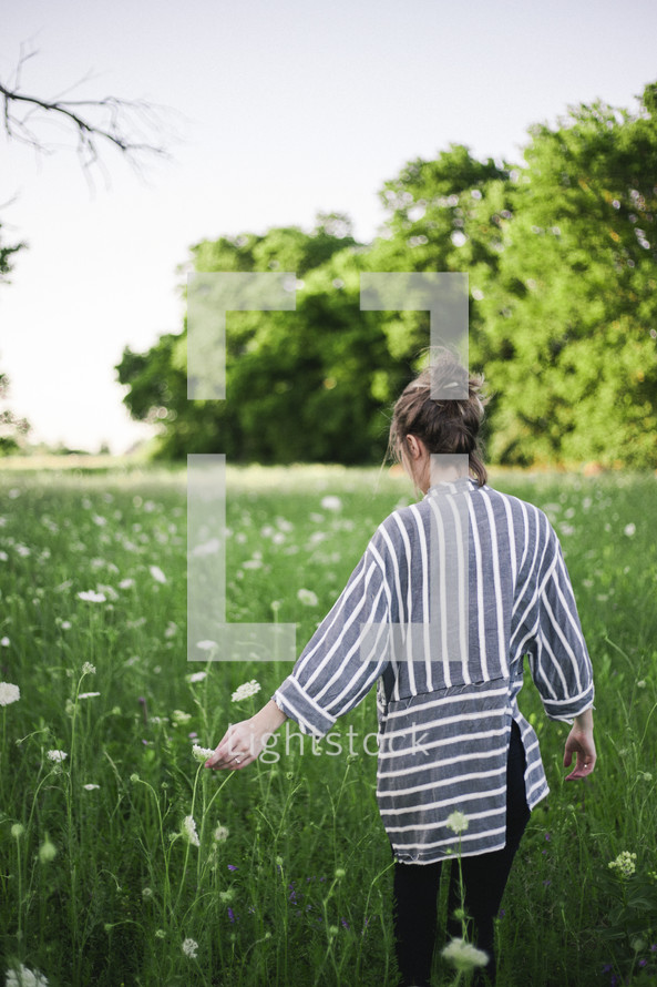 a woman walking through a field of wildflowers 