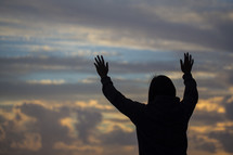 a woman with raised hands on at sunrise 