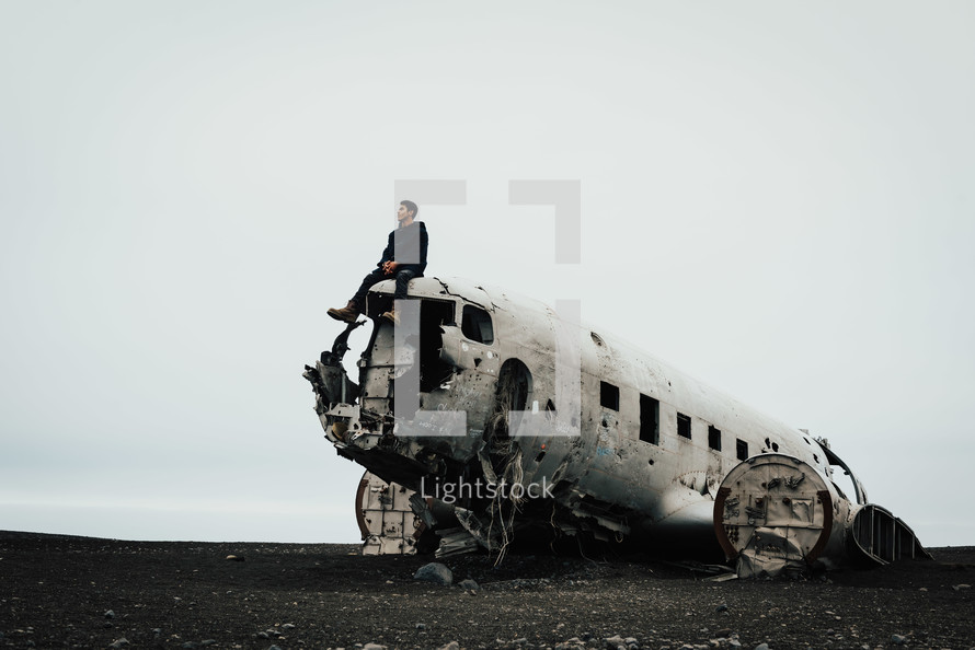 a man sitting on a wreckage of an airplane crash site 