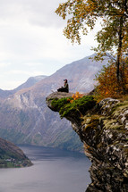 a woman sitting at the edge of a cliff looking out at the view 