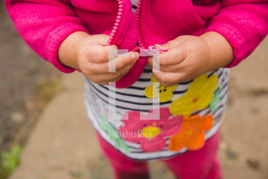 a toddler girl holding the zipper of her jacket 