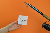 a hand reaching for a piece of paper with the word POWER on it hanging from a fishing line 
