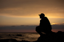silhouette of a man sitting on a shore 