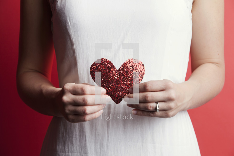 A woman in a white dress holding a paper heart 