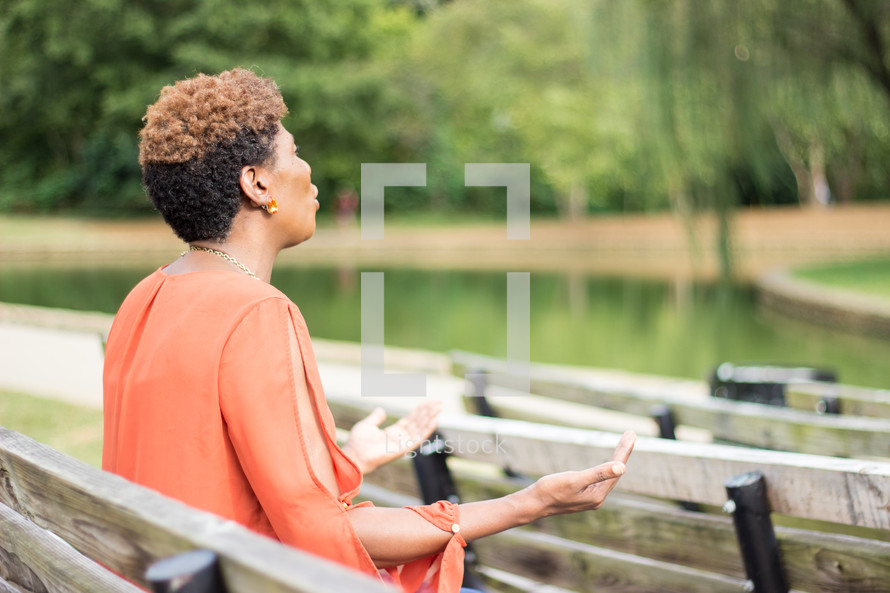 a woman sitting on a park bench with hands raised worshiping God 