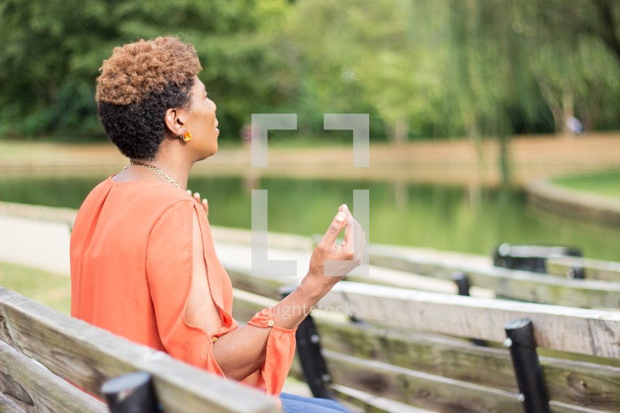 a woman sitting on a park bench with hands raised praying to God 