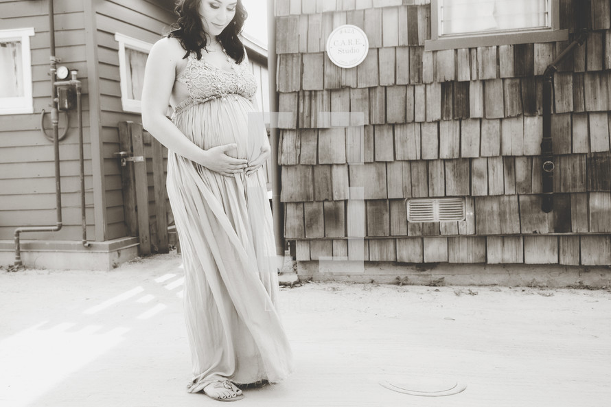 a pregnant woman standing in front of a house holding her belly