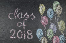 chalk on slate with balloons and the words: class of 2018