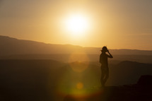 silhouette of a woman standing at the edge of a mountain at sunset 