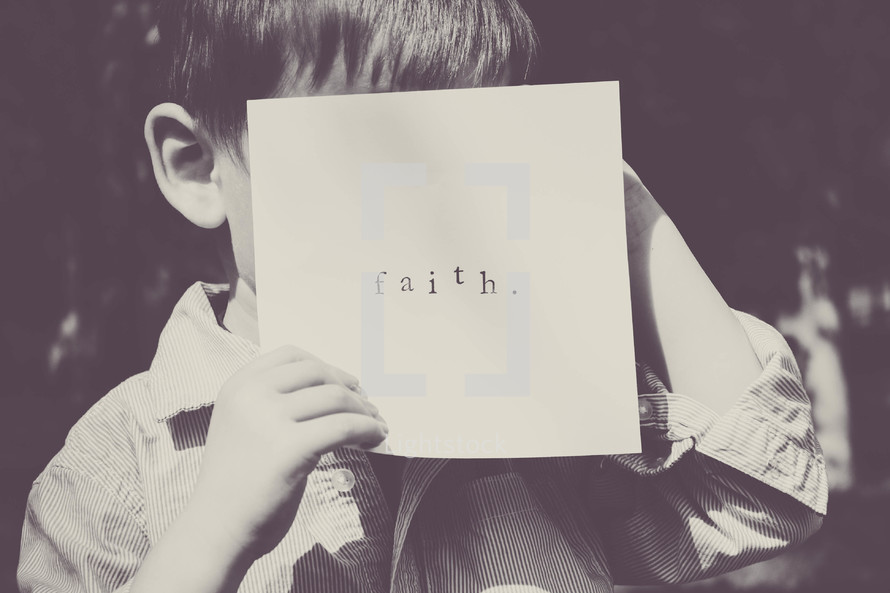 little boy hiding his face behind a piece of paper with the word faith 