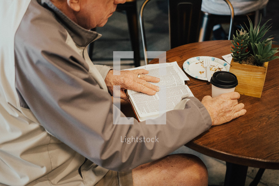 elderly man sitting at a table reading a Bible 