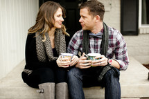 couple sitting on a step holding mugs of coffee 